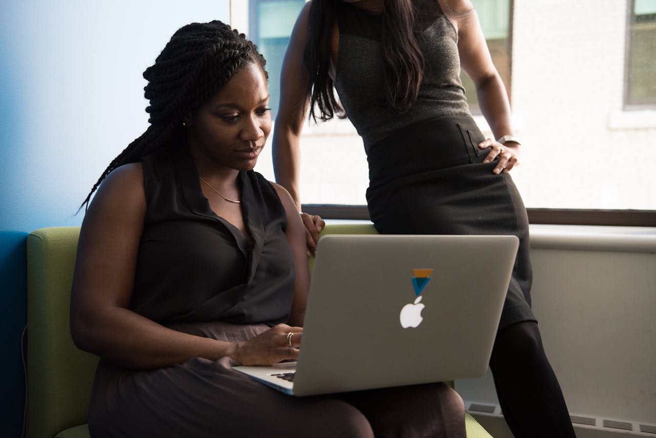 Two women working together on a laptop in a modern office setting.