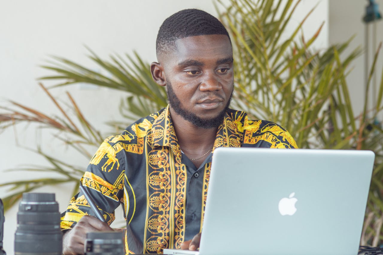 African man using a laptop outdoors with camera equipment in Douala, Cameroon.