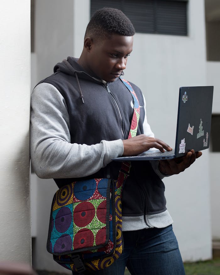 Young man using laptop outdoors in Accra, Ghana. Engaged in technology and learning.